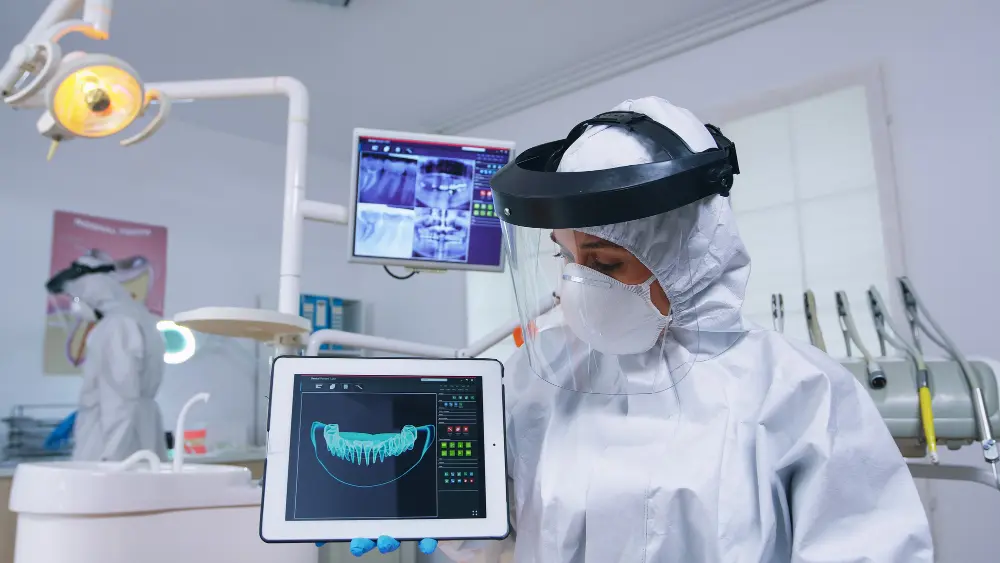 a woman wearing a white protective suit and face shield holding a tablet