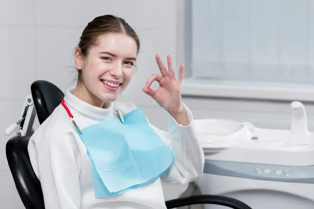 A smiling young woman sits in a dental chair, giving an "okay" sign. This image could convey the positive experience and satisfaction of a patient who has received quality orthodontic care. Choosing an experienced orthodontist, such as Limestone Hills Orthodontics in Austin, TX, can contribute to such a positive outcome.