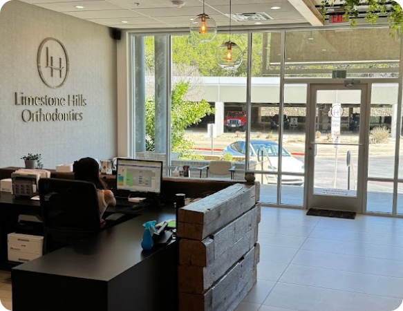 The reception area of Limestone Hills Orthodontics in Austin, TX, features a modern design with large windows and the clinic's logo.