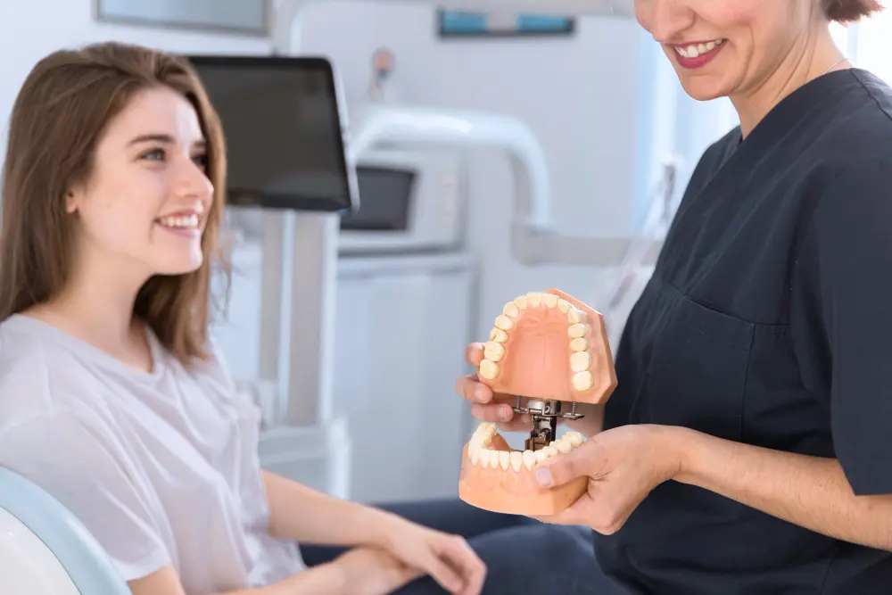 A dental professional, who appears to be a woman and may be of Caucasian descent based on her features, shows a teeth model to a smiling patient. Limestone Hills Orthodontics in Austin, TX, offers consultations.