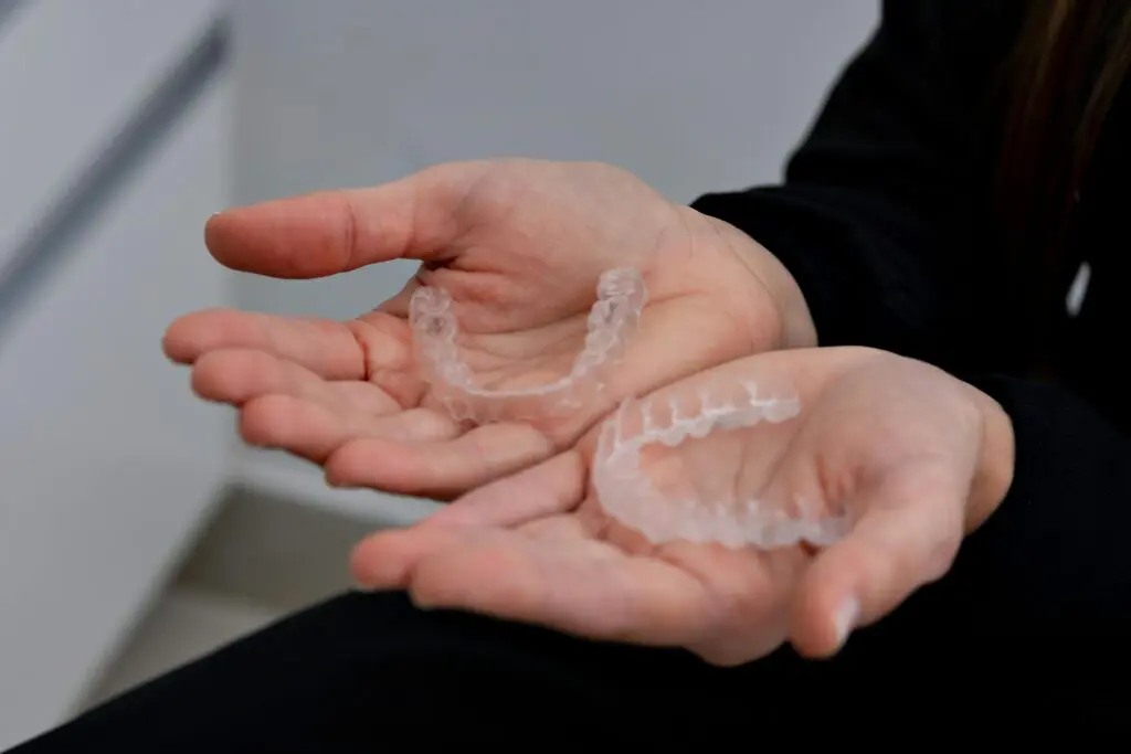 Two clear dental aligners are shown resting on open hands against a neutral background.