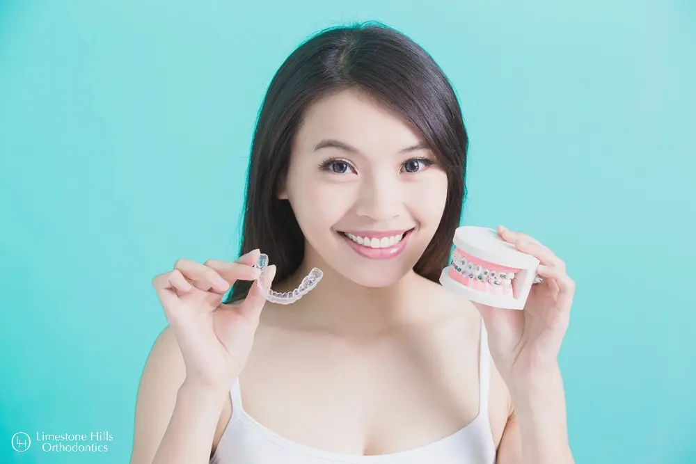 a woman holding a model of Invisalign and braces