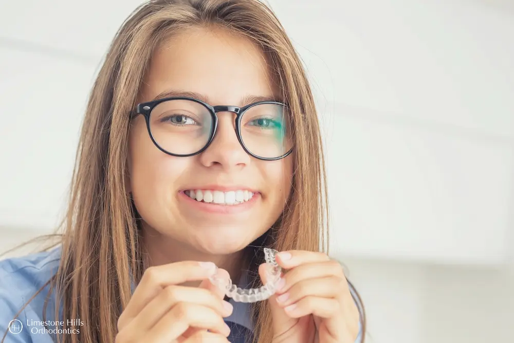 a girl smiling holding a clear plastic brace comparing Invisalign vs Angel Aligners