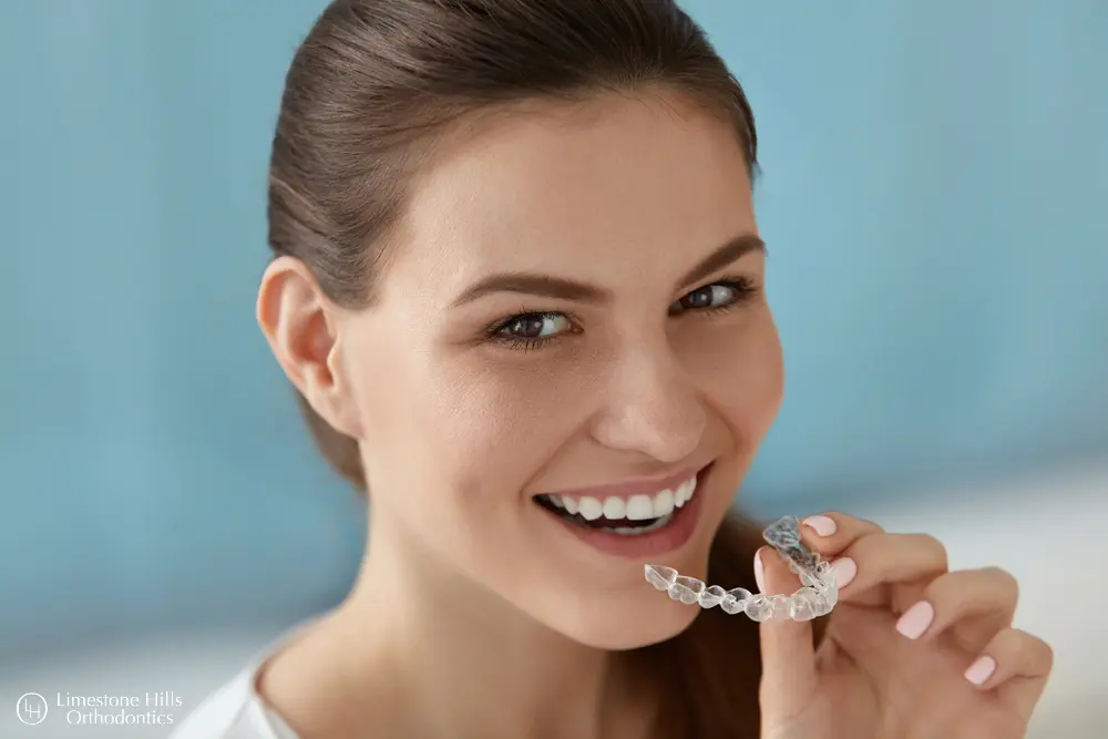 a woman smiling holding a clear plastic brace comparing Invisalign vs Angel Aligners