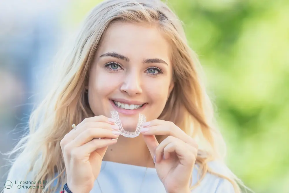 a woman smiling holding a clear Byte vs Invisalign aligner