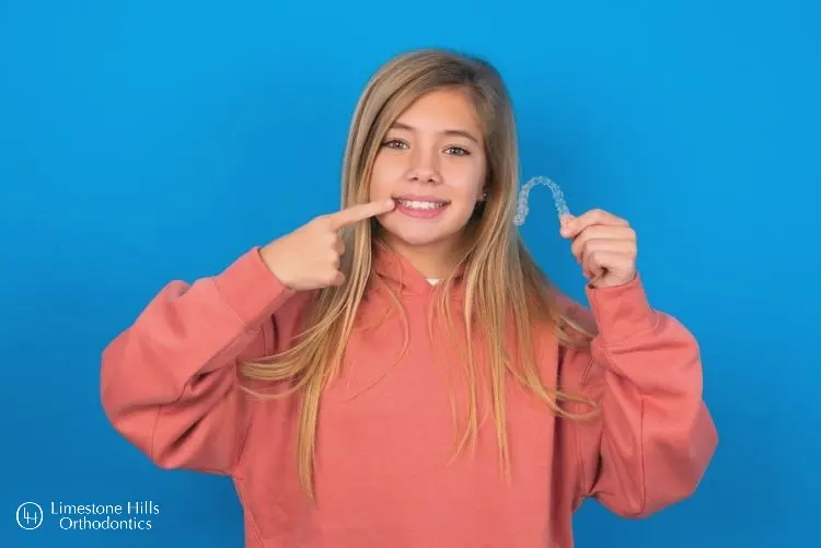 kids in Austin showing her teeth holding Invisalign. Invisalign for Kids