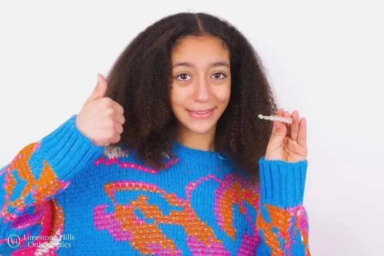 kids posing with her thumb up and holding Invisalign