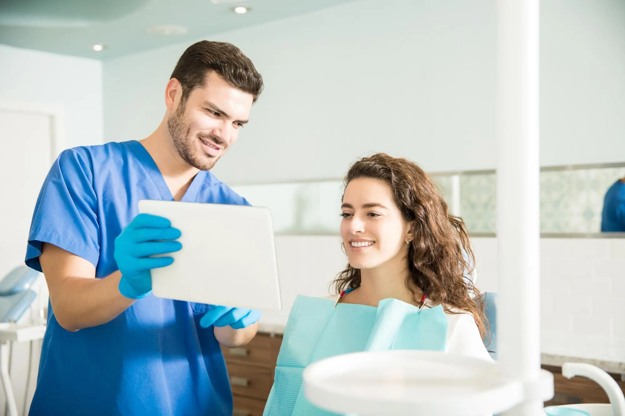At Limestone Hills Orthodontics in Austin, TX, a dentist in blue scrubs shows a tablet to a patient in a modern clinic.