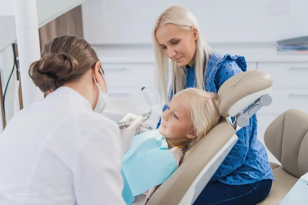 Mother watching an orthodontist take care of her young daughter’s teeth after keeping his daughter orthodontic treatment on track