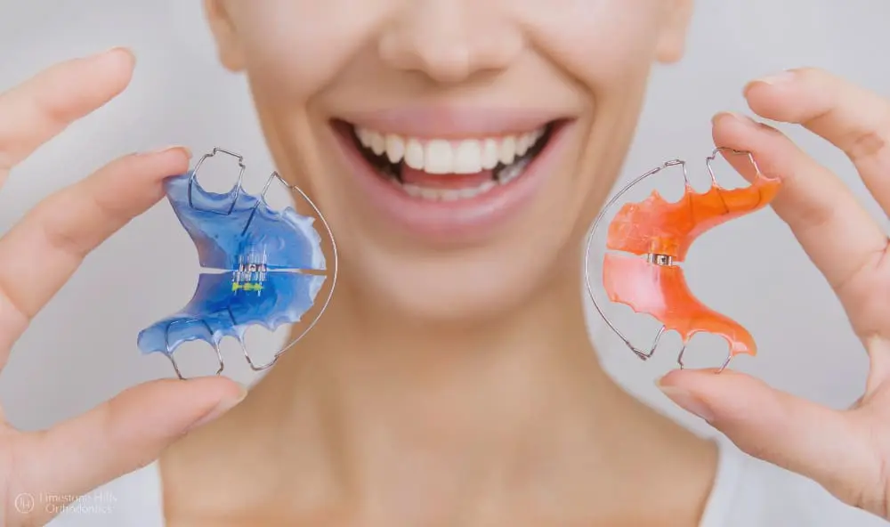 Beautiful smiling girl holding colorful retainers for teeth in a close-up shot after learning about the Importance of Wearing a Retainer.