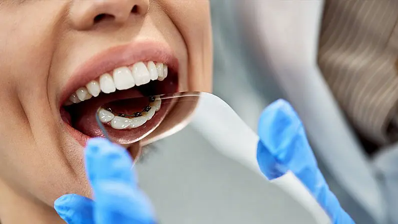 A close-up shows a patient's lower teeth with braces being examined using a mouth mirror. Limestone Hills Orthodontics in Austin, TX, provides orthodontic check-ups.