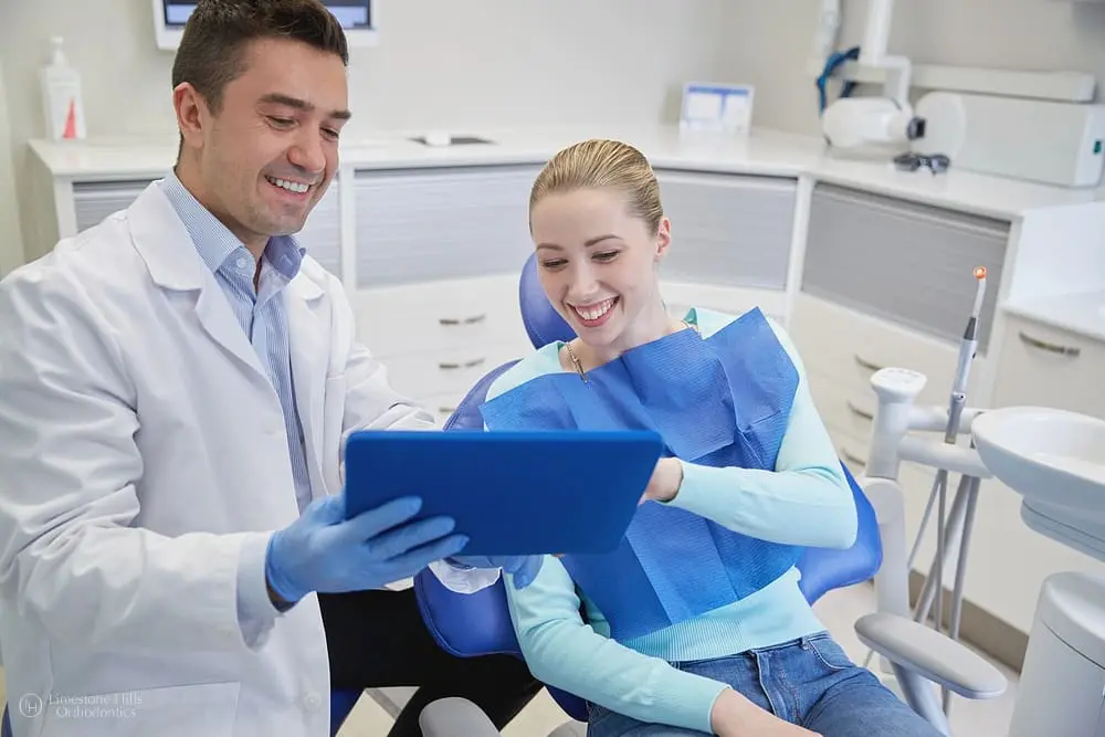 A dental professional, who appears to be a man and may be of Caucasian descent based on his features, shows a tablet to a smiling patient, who appears to be a young woman and may also be of Caucasian descent based on her features. Limestone Hills Orthodontics in Austin, TX.