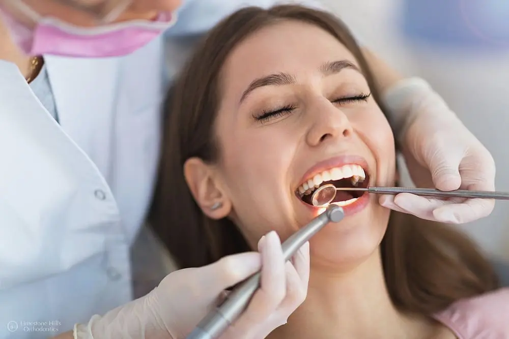 A patient, who appears to be a young woman and may be of Caucasian descent based on her features, receives a dental cleaning. Limestone Hills Orthodontics in Austin, TX.