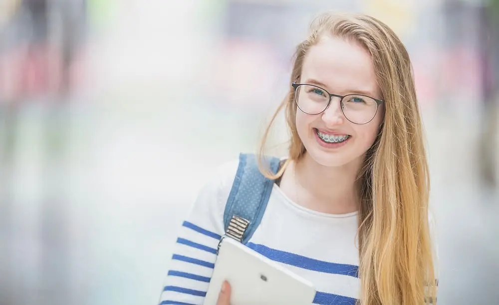 Portrait of a smiling, beautiful teenage school girl being back to school with braces, outdoors with blurred background
