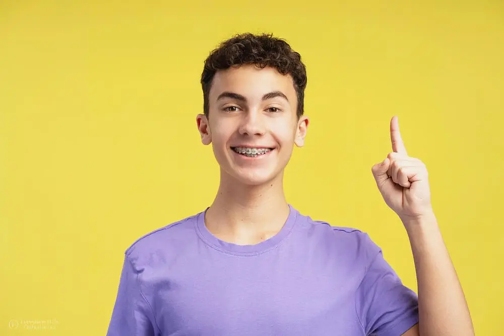 Portrait of a smiling, excited boy with metal braces, wearing a casual t-shirt and pointing upwards as he explain about holiday tips for braces