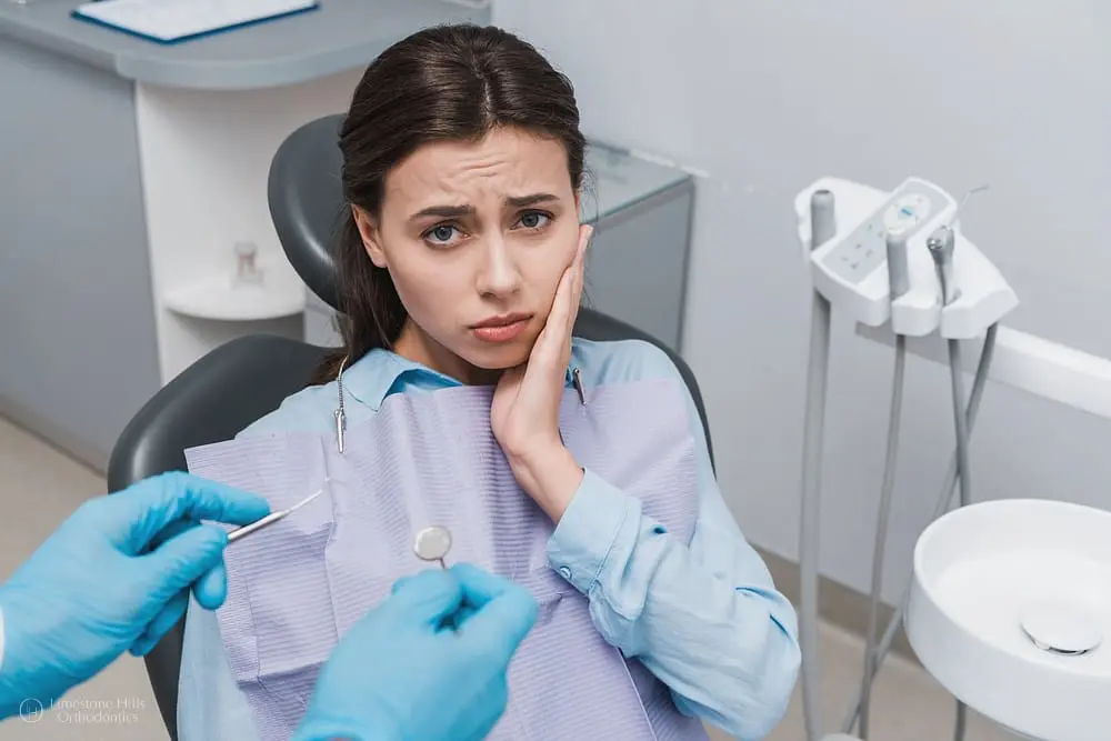 Upset woman sitting in a dental chair while a dentist wearing latex gloves holds dental instruments after Choosing the Best Orthodontic Treatment.