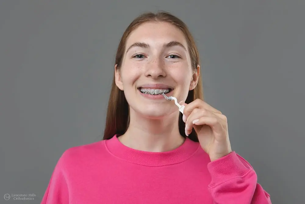 Teenage girl with metal braces cleaning her teeth with an interdental brush, answering the question "can braces stain my teeth?"