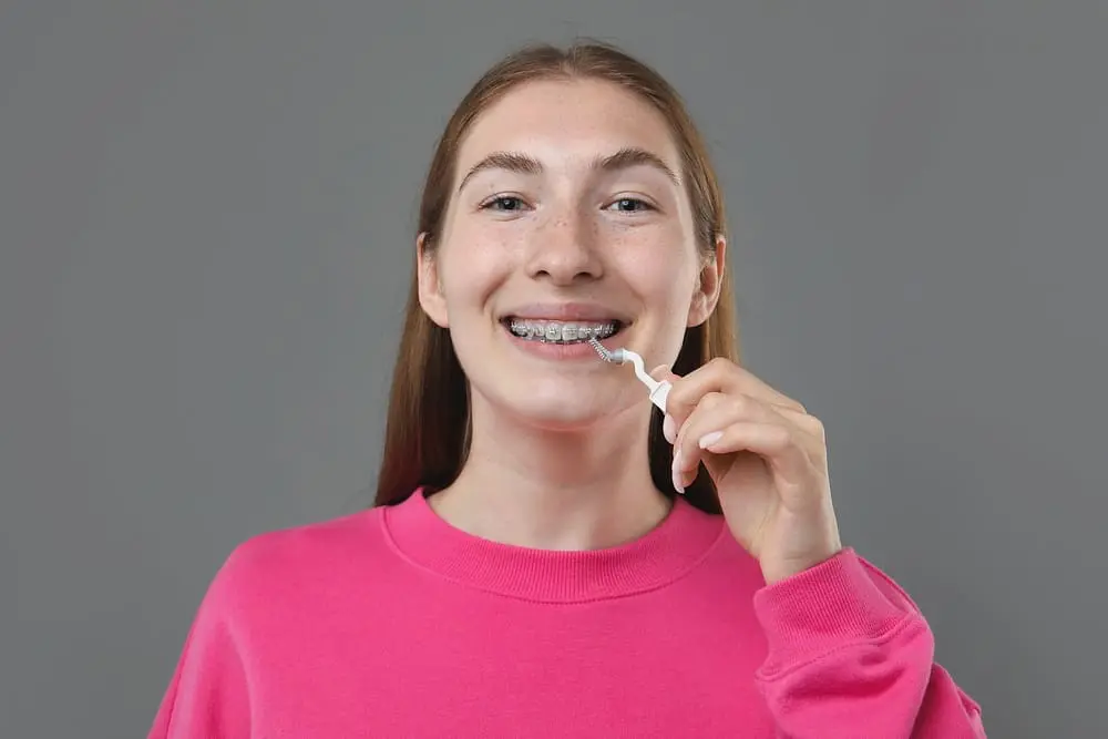 Teenage girl with metal braces cleaning her teeth with an interdental brush, answering the question "can braces stain my teeth?"