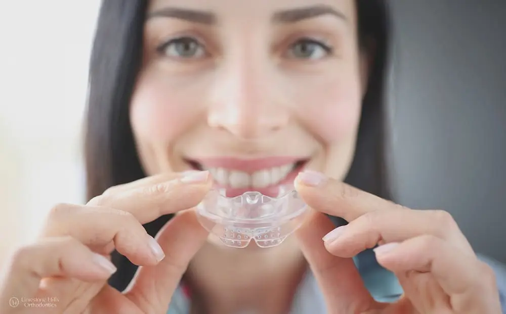 Smiling woman holding sports mouthguard for braces close to her teeth