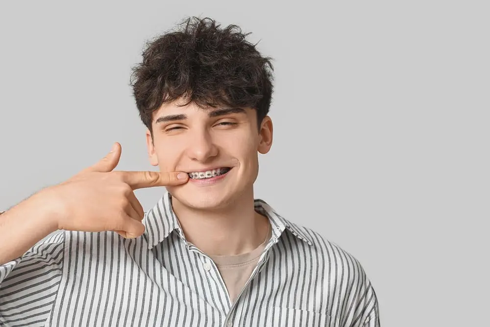 smiling young man metal braces light background after asking about "Will Braces Change My Face Shape?"