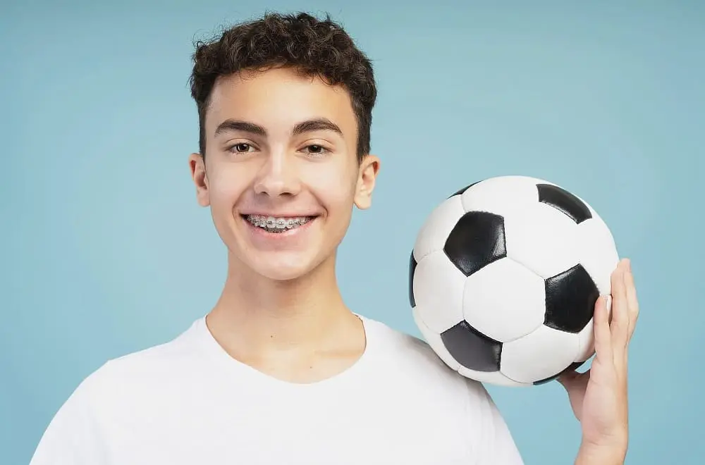 Young man in a white t-shirt holding a soccer ball and smiling after purchasing sports mouthguard for braces
