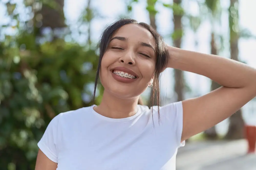 Young woman with metal braces, breathing deeply with closed eyes, standing outdoors after knowing about Summer Survival Guide for Braces