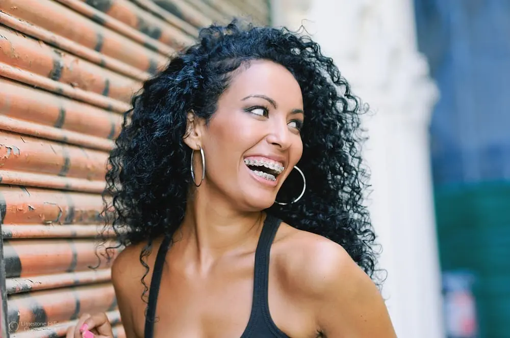 Young Black woman smiling with metal braces, looking joyful in an outdoor setting after knowing about Facts About Adult Orthodontics