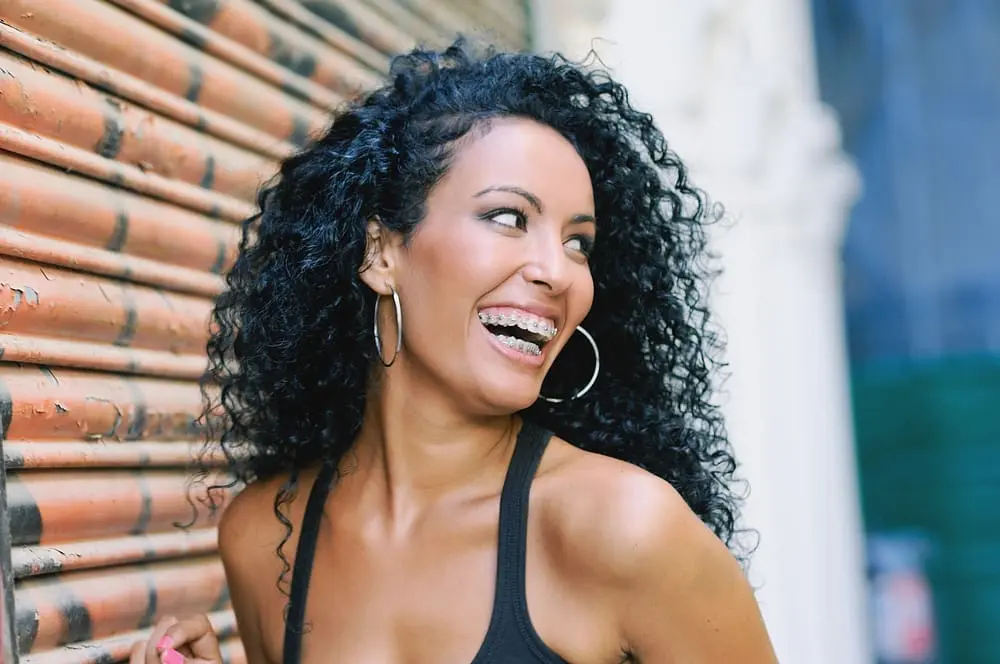 Young Black woman smiling with metal braces, looking joyful in an outdoor setting after knowing about Facts About Adult Orthodontics