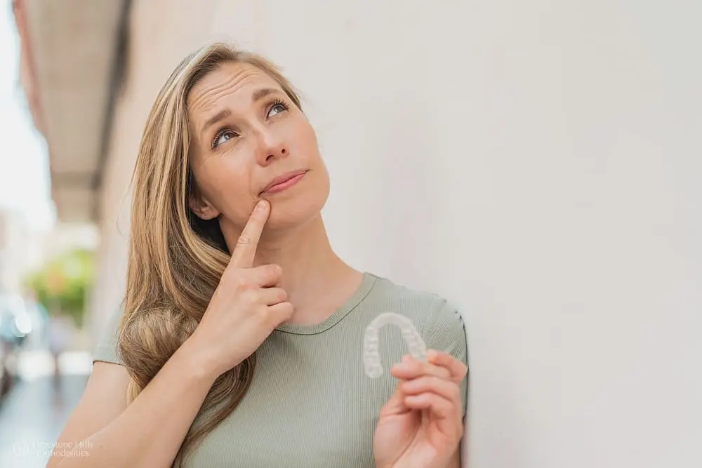 Young blonde woman outdoors holding Invisalign clear aligners and wondering about tips to avoid invisalign irritation