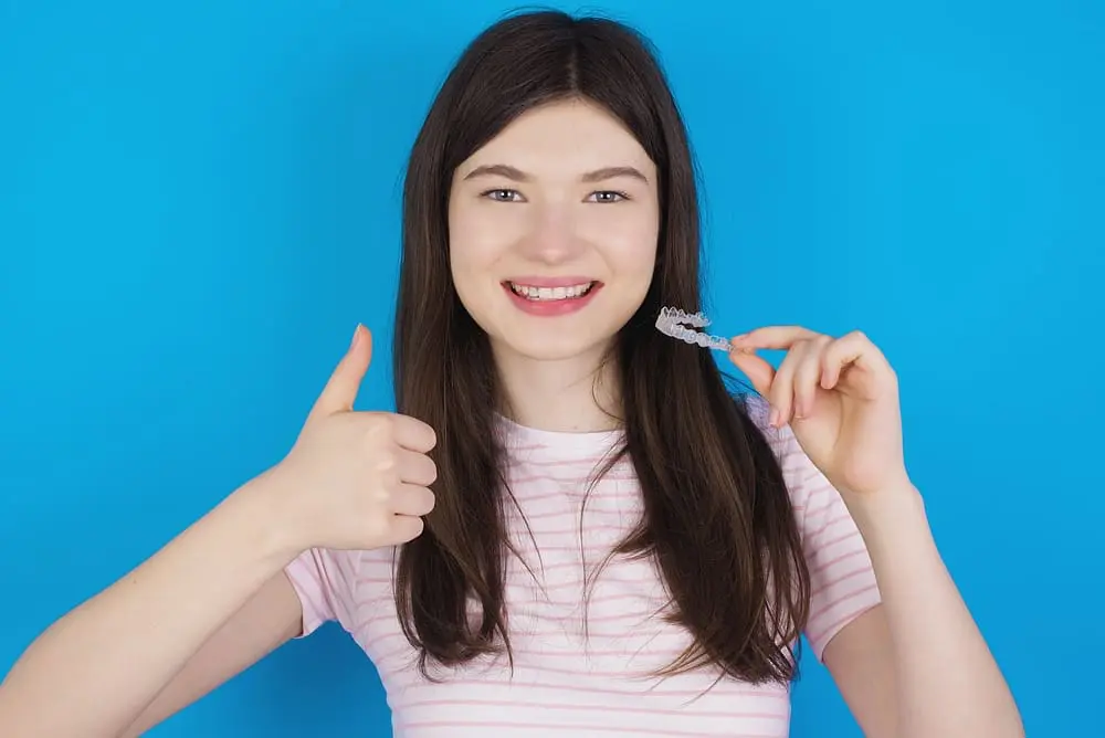 Brunette woman smiling while holding Invisalign attachments clear aligners.