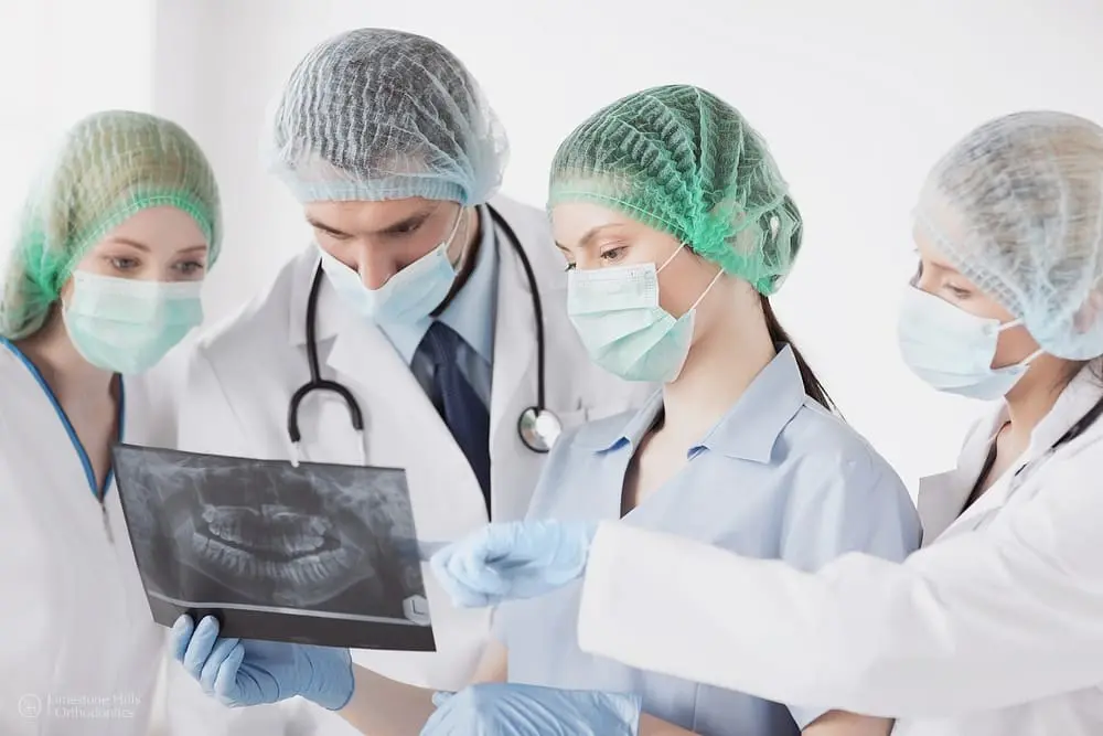 Group of orthodontists looking at a dental X-ray together in a clinic setting to investigate the causes of crooked teeth