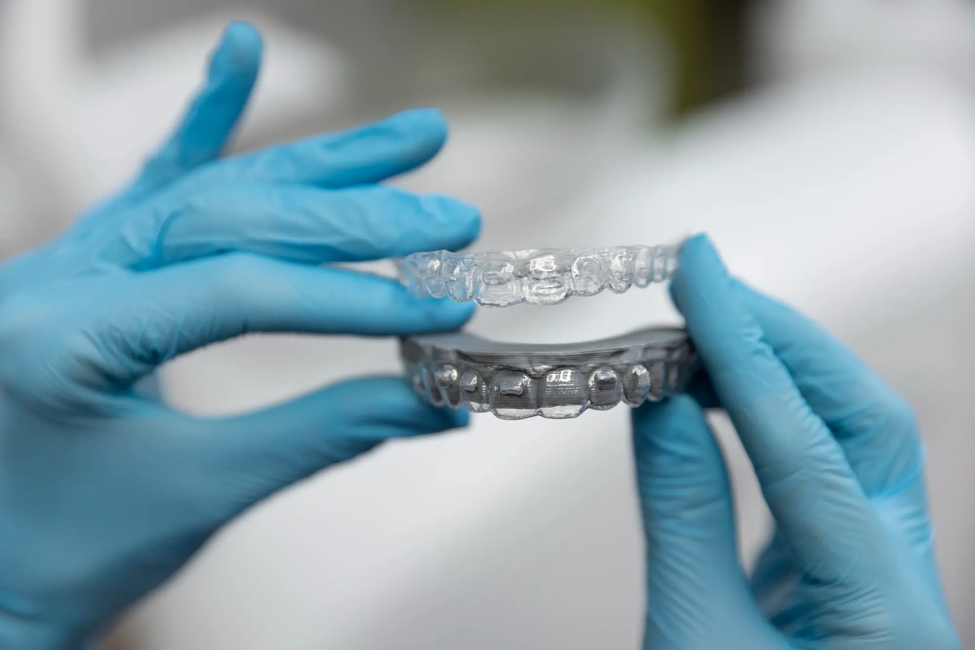 A person in blue gloves holds clear aligners. Could be Invisalign. Limestone Hills Orthodontics, Austin, TX.