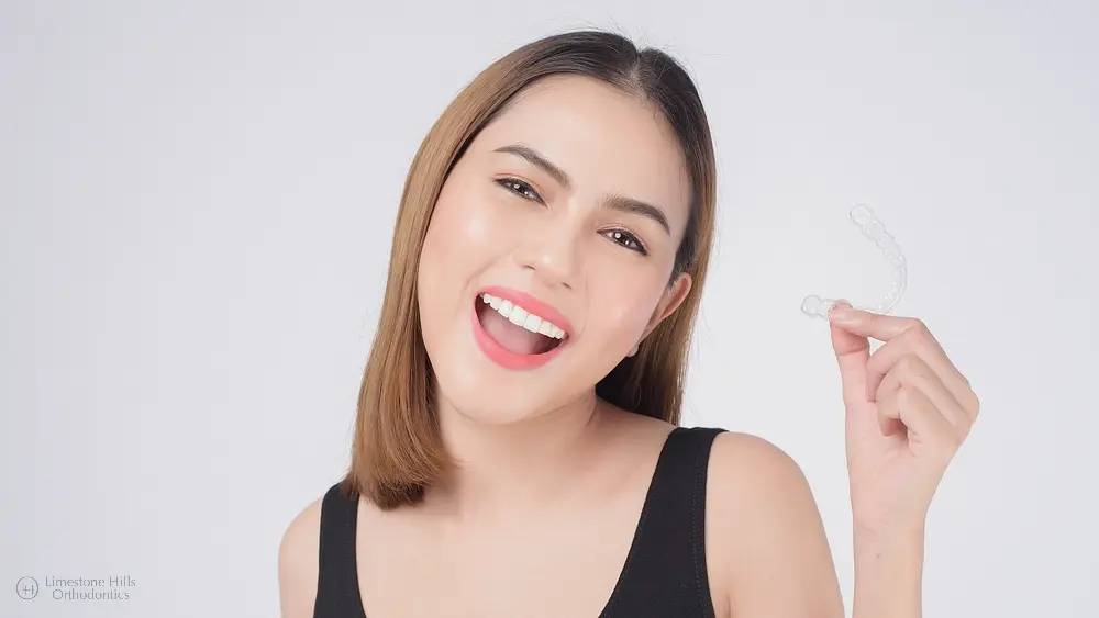 A smiling woman holding a clear aligner, showcasing a discreet method on how to fix overbite in austin tx at home.