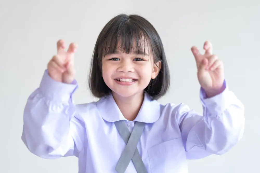 A smiling teenage girl with metal braces playfully making a bunny gesture, highlighting the aesthetic and social implications of braces. Limestone Hills Orthodontics in Austin, TX, provides supportive orthodontic care.