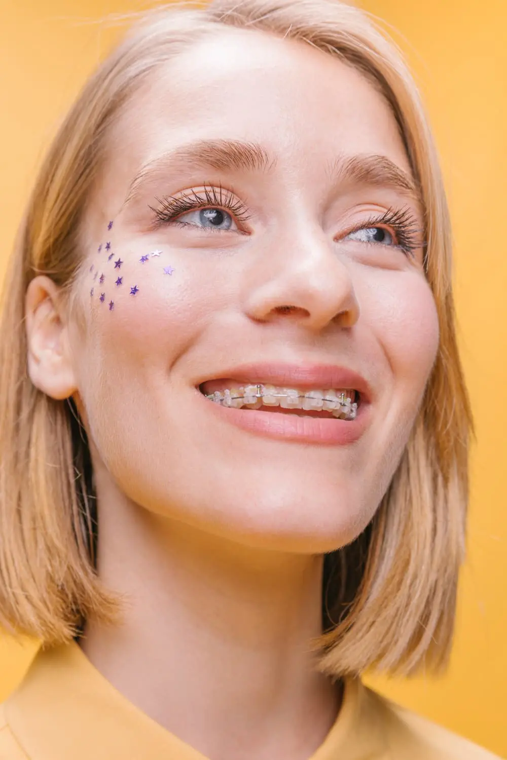A teen or adult smiling with clear ceramic braces against a yellow background, highlighting a discreet orthodontic option. Limestone Hills Orthodontics in Austin, TX, offers clear braces for both teens and adults.