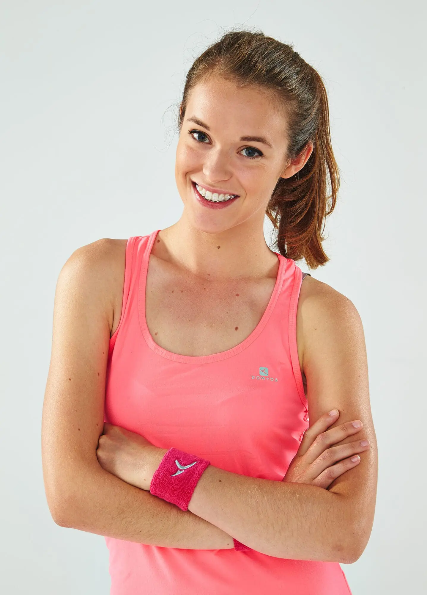 Smiling young woman with crossed arms wearing self-ligating clear ceramic braces at Limestone Hills Orthodontics in Austin, TX.