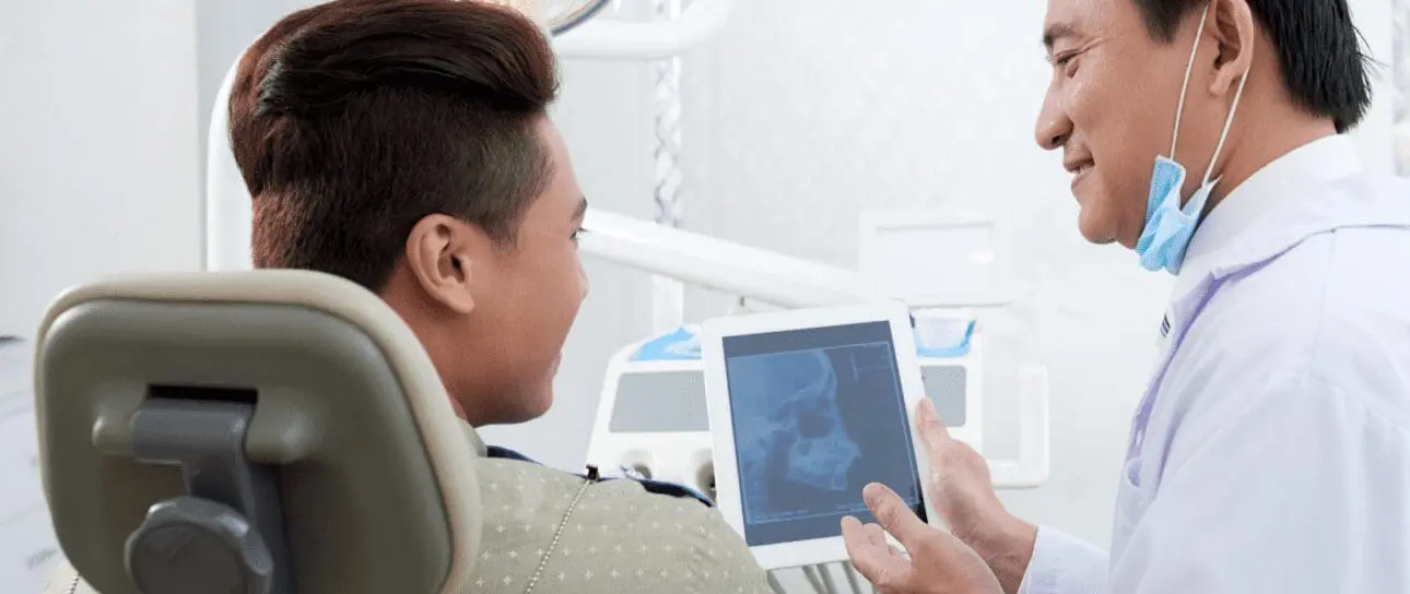 Dentist showing a patient an X-ray on a tablet while explaining Rehabilitation Exercises during Jaw Surgery recovery at Limestone Hills Orthodontics in Austin, TX.