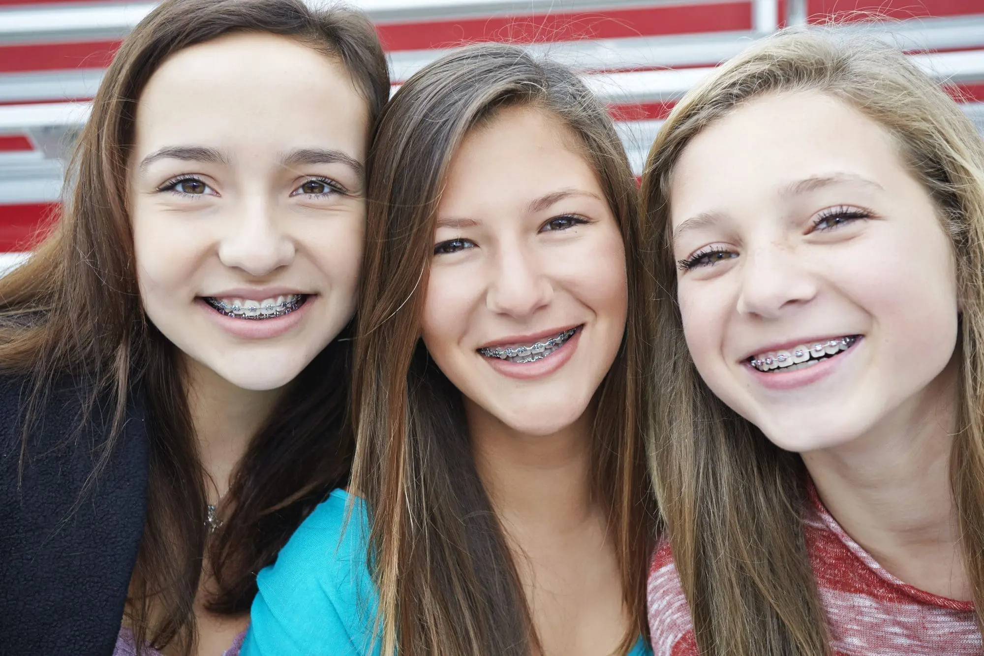 Three smiling teenage girls showing their colorful elastic braces, highlighting the fun and customization options of metal braces. Limestone Hills Orthodontics in Austin, TX, provides expert teen orthodontic care.