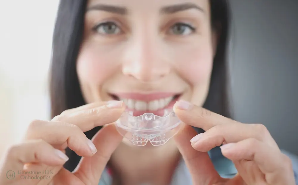 Smiling woman placing a clear Invisalign aligner on her teeth as one of the dental orthotics in Austin, TX