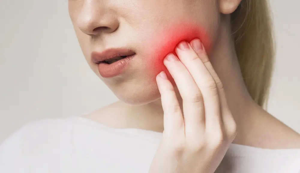 Woman holding her cheek in pain with visible red highlight indicating smile concerns solved by orthodontic in Austin, TX