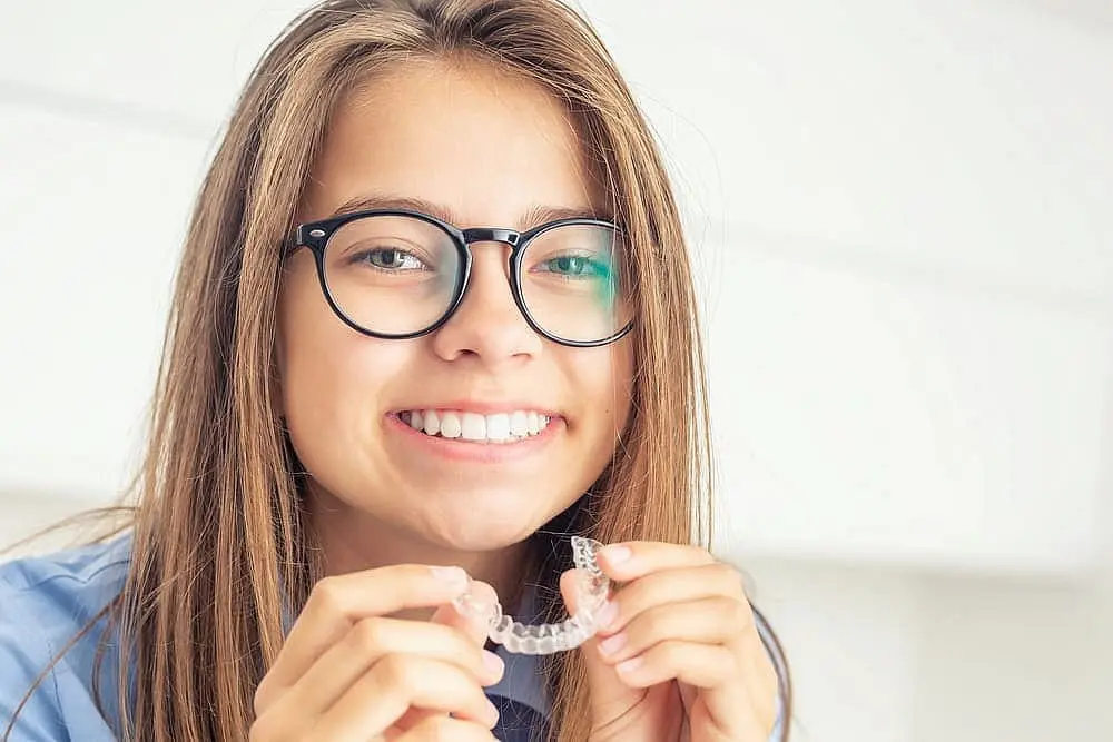 Young girl holding clear aligners at Limestone Hills Orthodontics in Austin, TX for early orthodontic treatment