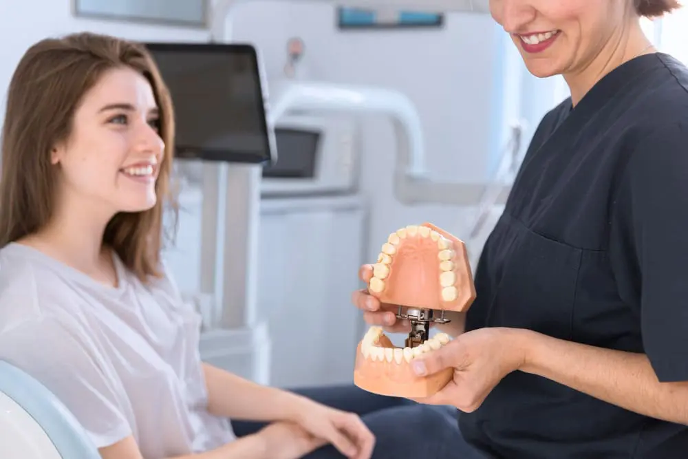 A female dental professional showing a teeth model to a smiling adult patient, highlighting important considerations for adult braces. Limestone Hills Orthodontics in Austin, TX, provides expert orthodontic consultations.
