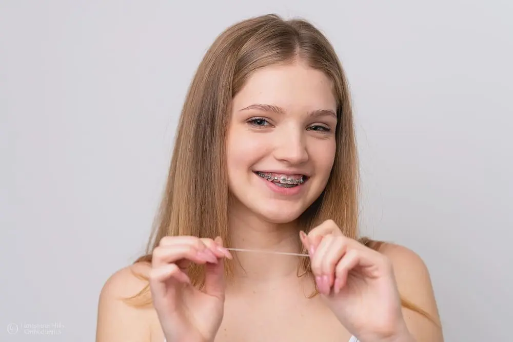 Smiling woman with traditional braces holding elastics at Limestone Hills Orthodontics, adult orthodontics in Austin, TX
