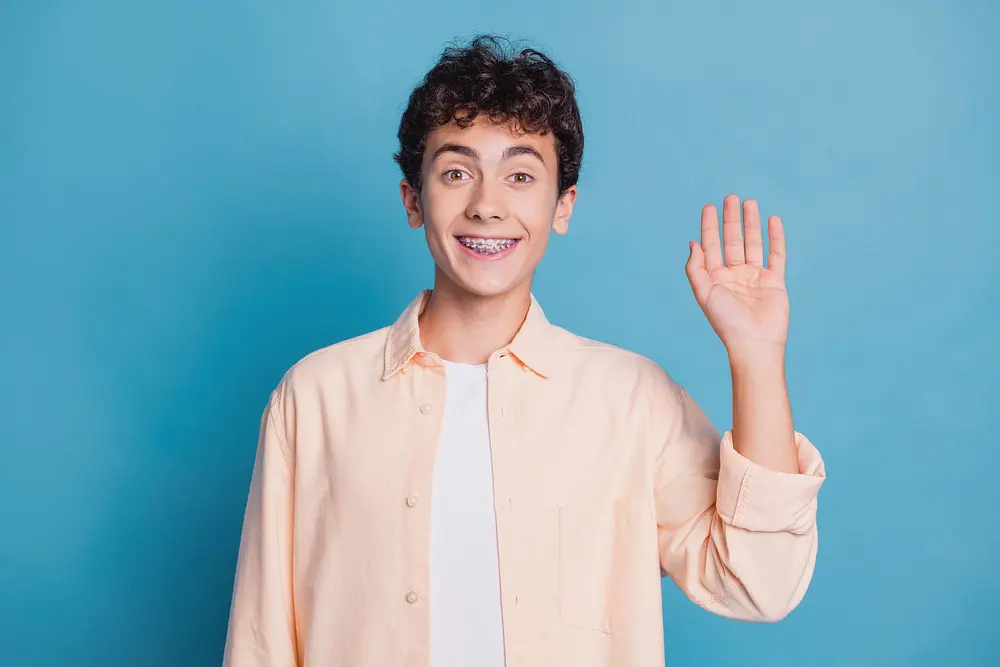 Teenage boy with braces smiling for Limestone Hills Orthodontics after his tooth alignment in Austin, TX, on a blue background.