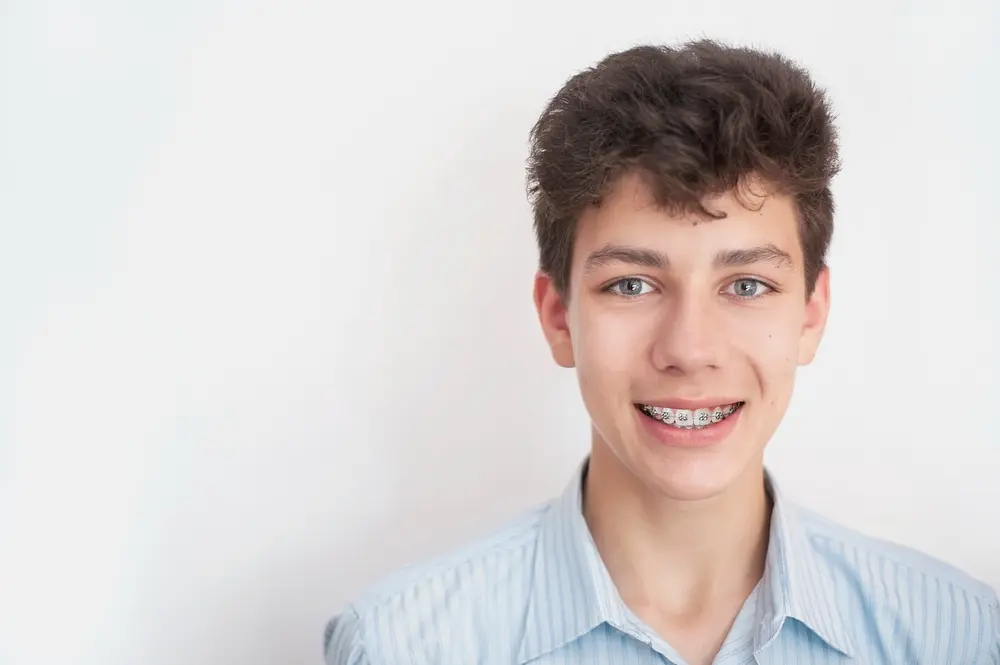 Teenage boy with braces smiling for Limestone Hills Orthodontics after his tooth alignment in Austin, TX, on a white background.