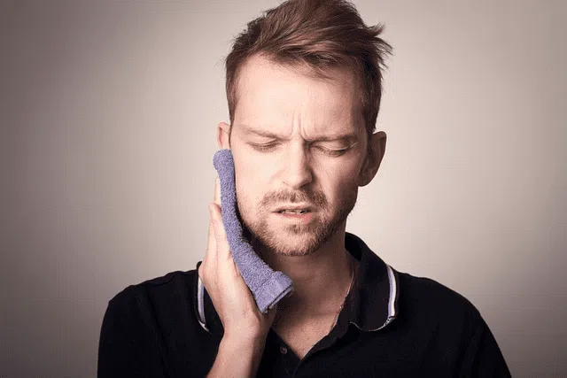 A man with a concerned expression holds a cold compress to his jaw, suggesting potential discomfort related to a malocclusion such as an overbite. This image could represent the need for treatment methods to fix an overbite, offered by Limestone Hills Orthodontics in Austin, TX.